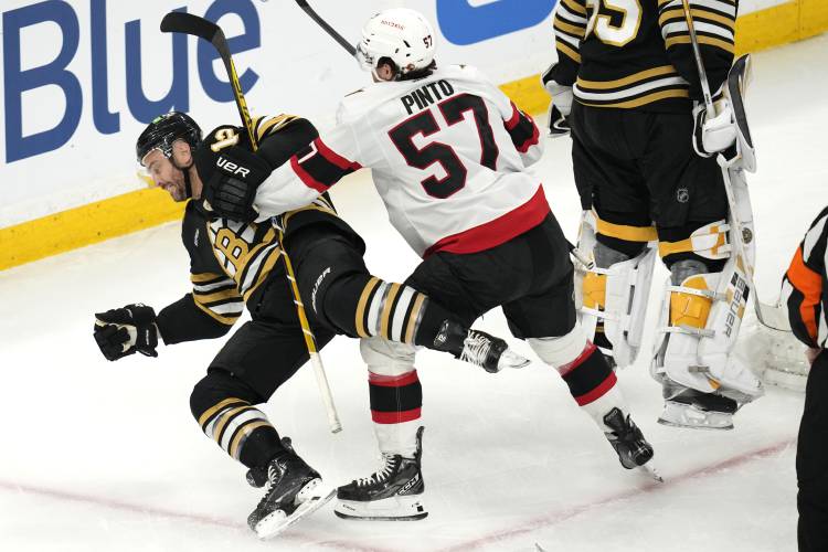 Boston Bruins defenseman Kevin Shattenkirk, left, is knocked to the ice by Ottawa Senators center Shane Pinto (57) during the first period of an NHL hockey game Tuesday, April 16, 2024, in Boston. (AP Photo/Charles Krupa)