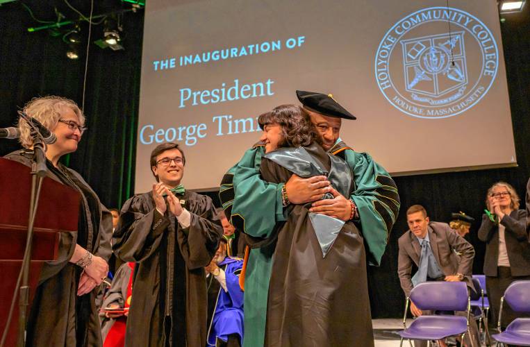 Vanessa Smith, Holyoke Community College interim chair of the board of trustees, left, and student trustee Barney Garcia, look on as George Timmons receives a hug from student Alicia Beaton as Timmons is installed as the fifth president of Holyoke Community College during an inauguration ceremony in Holyoke on Friday, April 19, 2024.