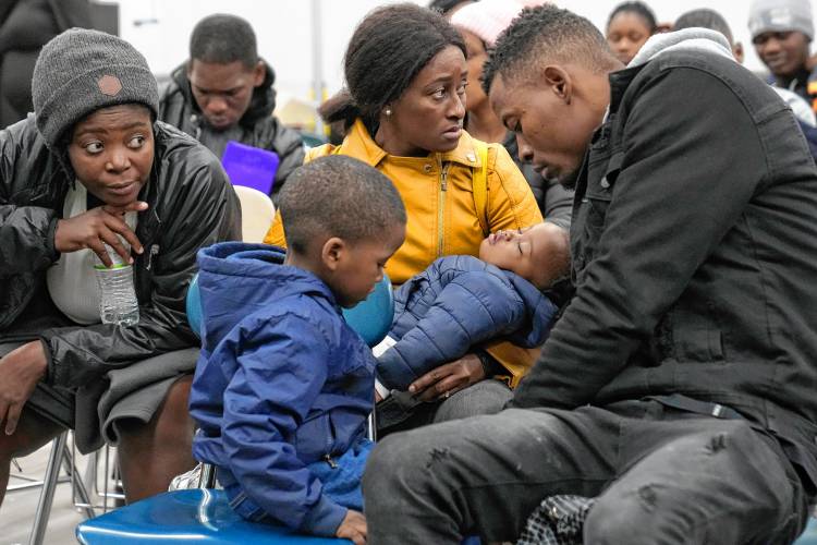 Petterly Jean-Baptiste and his wife, Leonne Ysnardin, behind center, immigrants from Haiti, wait with their two children on Nov. 16 at the Immigrant Family Services Institute in the Mattapan neighborhood of Boston for transportation to a shelter in Quincy.
